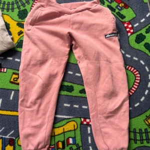 Rosa mjukisbyxor från Ellesse - Snygga rosa mjukisbyxor från Ellesse med resår i midjan och benslut. Byxorna har sidofickor och en broderad Ellesse-logga på benet. Tillverkade i mjukt bomullsmaterial som är skönt mot huden. Perfekta för chill dagar eller när du vill vara bekväm.