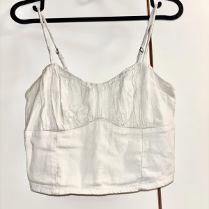 Vit linnetopp från Hollister - Supersöt vit linnetopp från Hollister med smala justerbara axelband och lätt rynkad byst. Toppen har smockad rygg för extra komfort och sitter croppad 🤍