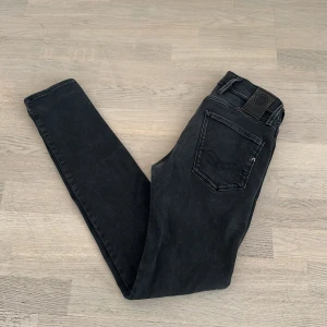 Replay Anbass 28/32 - Svarta Replay Anbass jeans med smal passform och klassisk femficksdesign. Jeansen har en snygg tvättad look, normal midja och raka ben. Tillverkade i stretchig denim för extra komfort. Perfekta för dig som gillar stilrena och moderna jeans.