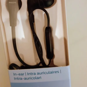 Philips TAE1105 In-ear Headphones with Mic - Nya Philips TAE1105 in-ear hörlurar med mikrofon, 1000-serien. Ger kraftfull bas och bekväm passform. Perfekt för samtal och musik. Produkten är i originalförpackning och ser helt oanvänd ut, utan synligt slitage eller defekter.
