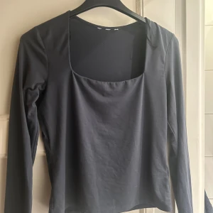 Mörkgrå långärmad topp med fyrkantig hals - Snygg mörkgrå långärmad topp med en modern fyrkantig halsringning. Tillverkad i mjuk bomull som känns skön mot huden. Enkel och stilren design som är lätt att matcha med olika outfits. Perfekt för dig som gillar minimalistisk stil.