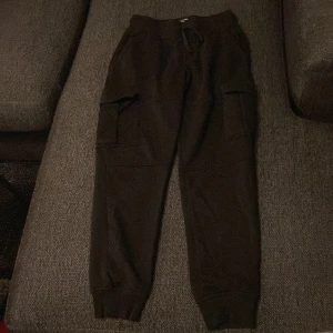 Svarta cargopants med snörning - Svarta cargopants med bekväm snörning i midjan och stora fickor på sidorna. Byxorna har ribbade muddar vid bensluten och är gjorda i mjukt material som passar chill och streetwear. Perfekt för dig som gillar avslappnad stil.