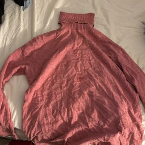 Rosa polotröja med ribbad krage - Mysig rosa polotröja med bred, ribbad krage och långa ärmar. Tröjan har en loose passform och är tillverkad i ett mjukt stickat material som känns skönt mot huden. Perfekt för att hålla värmen under kyliga dagar.