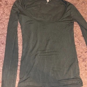 Mörkgrön långärmad topp - Säljer en enkel och stilren mörkgrön långärmad topp med rundad halsringning. Toppen har en tight passform och är tillverkad i mjukt bomullsmaterial som känns skönt mot huden. Perfekt att matcha med jeans eller kjol för en clean look.