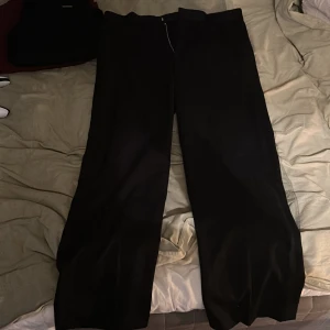 Svarta wide kostymbyxor från H&M - Svarta kostymbyxor från H&M i relaxed fit med wide ben. Klassisk design med dragkedja och knapp framtill. Perfekt för dig som gillar en chill och stilren look. Materialet känns mjukt och har en snygg fall.