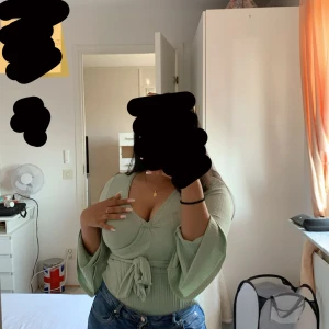 Ljusgrön omlottopp från Boohoo - Snygg ljusgrön omlottopp från Boohoo med ribbad struktur och långa trumpetärmar. Toppen har v-ringning, knyt i midjan och är en body. Perfekt att styla med jeans eller kjol för en trendig look.