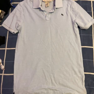 Ljusblå pikétröja från H&M L.O.G.G. - Ljusblå pikétröja från H&M L.O.G.G. med klassisk krage, korta ärmar och knappslå framtill. 