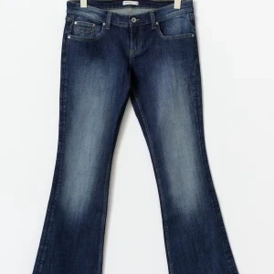 Blå bootcut jeans med broderade fickor - Snygga blå bootcut jeans med coola broderade detaljer på bakfickorna. Jeansen har klassisk femficksdesign, knapp och dragkedja fram samt lätt slitna partier för en schysst vintagekänsla. Perfekt passform och skön stretch i materialet. även väldigt lågmidjade för dom som gillar det, helt oanvända och prislapp sitter kvar på jeansen