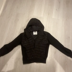 Svart pufferjacka med huva från Zara - Snabb leverans.   Jackan säger att den är L men jag tycker det är M så snälla ta Hansyn.   Svart pufferjacka från Zara med huva och quiltad framsida. Jackan har dragkedja, långa ärmar och en clean look. Materialet är en mix av polyester och syntet, vilket gör den lätt och skön. Perfekt för dig som gillar streetstyle och vill ha en jacka med snygg passform.