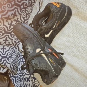 Nike Air Max svarta sneakers med orange detaljer - Svarta Nike Air Max sneakers med orange logga och detaljer. Skorna har klassisk snörning, vit swoosh på sidan och meshpaneler för extra andningsförmåga. Snygg och sportig look med platt sula och rund tå. Perfekta för dig som gillar streetstyle och komfort. Lite slita inne se bilder. Fina utanpå. Har mycket kvar att ge