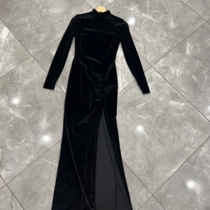 Oanvänd svart sammetslångklänning  - Elegant svart långklänning i mjuk sammet med lång ärm och hög hals. Klänningen har en snygg drapering framtill och en slits. Den är helt oanvänd och köpt från NLY eve. 