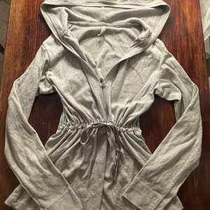 Grå babydoll huvtröja - Grå hoodie med en superfin rosett som knyts kring midjan 💕 Den är i storlek S, men passar även XS-M. Den har en luva i perfekt storlek. Knappar kan knäppas vid bröstet, vid knytbandet och under knytbandet! Tröjan är väldigt bekväm och mjuk, eftersom den är 100% bomull 🤍