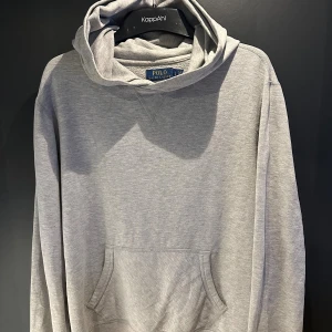 Grå hoodie från Polo Ralph Lauren - Snygg grå hoodie från Polo Ralph Lauren med klassisk huva. Tröjan har lång ärm och är tillverkad i mjuk bomullsmix som känns skön mot huden. Perfekt för chill dagar och enkel att matcha med jeans eller joggers.