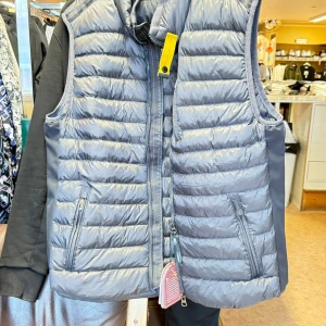 Grå dunväst från Parajumpers  - Snygg grå dunväst från Parajumpers i storlek XXL. Västen har quiltad design, dragkedja framtill, två fickor med dragkedja och en gul detalj vid kragen. Perfekt för lager-på-lager och riktigt skön att bära under kyliga dagar.