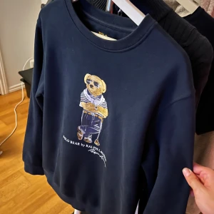 Polo Bear Ralph Lauren Mörkblå - Mörkblå sweatshirt från Polo Ralph Lauren med ikoniska Polo Bear-trycket på bröstet. Tröjan har rund hals, lång ärm och en relaxed passform. Materialet är mjuk bomull som känns skönt mot huden. 