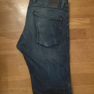 Replay Anbass jeans blå tapered - Säljer ett par blå Replay Anbass jeans med snyggt tvättad look och klassisk femficksdesign. Jeansen har tapered passform som sitter skönt och ger en modern siluett. Materialet är slitstarkt jeans och de har detaljerade sömmar på bakfickan.