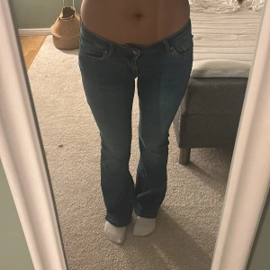 Blå bootcut jeans låg midja - Snygga blå jeans med bootcut passform och låg midja. Klassisk femficksmodell med subtila slitningar och kontrastsömmar. Jeansen har en smickrande siluett som sitter tajt över låren och släpper ut vid vaden. Perfekta för en chill och trendig look.