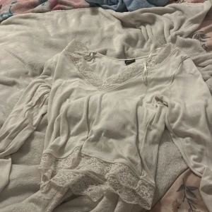 Vit blus med spetsdetaljer - Säljer en söt vit blus från Gina Tricot med v-ringning och spetsdetaljer vid halsen och nederkanten. Blusen har långa ärmar och en liten knytning vid halsen. Perfekt för dig som gillar romantisk stil och mjuka material. Använd endast fåtal gånger lite för stor för mig då jag har storlek xss men köptes för 299 säljer för 120 storlek M men passar S skulle jag nog kunna säga 