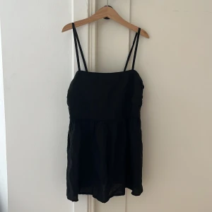 Svart blus från Lindex - Svart blus från Lindex i storlek XS med tunna axelband och luftig, rynkad kjoldel. Enkel och stilren design som passar dig som gillar minimalistiskt. Materialet känns lätt och bekvämt, perfekt för varma dagar. Säljes då den inte längre kommer till användning.