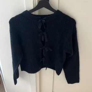 Mörkblå stickad kofta med rosetter Gina Tricot - Mysig mörkblå stickad kofta från Gina Tricot med långa ärmar och snygga knytrosetter framtill. Perfekt för lager på lager och ger en cool touch till din outfit. Tjockt garn och klassisk rund halsringning.