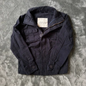 Marinblå fieldjacket - Marinblå fieldjacket med coola fickor framtill och broderad logga på ärmen. Dragkedja och hög krage i slitstark bomull. Riktigt fet field jacket – tyvärr passar den inte på mig.