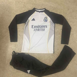 Real Madrid långärmad fotbollströja Adidas - Säljer en långärmad Real Madrid fotbollströja från Adidas i vit och svart med gula detaljer. Tröjan har klubbmärke och sponsortryck på bröstet samt dragkedja vid halsen. Materialet är lätt och andas, perfekt för träning eller match.