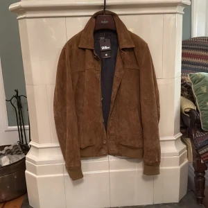 Oscar Jacobson mockajacka  - Snygg brun mockajacka från Oscar Jacobson i klassisk bombermodell. Jackan har krage, knäppning framtill och ribbade muddar vid ärmslut och midja. Perfekt för dig som vill ha en stilren och tidlös look med premiumkänsla. Aldrig använd och ny med tags. Butikspriset ligger på 8000kr. Storlek 48 motsvarar M/S. 