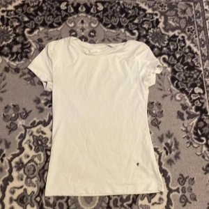 Vit basic t-shirt från H&M - Enkel vit t-shirt från H&M i storlek S. Klassisk modell med rund hals och korta ärmar, tillverkad i mjuk bomull. Perfekt till jeans eller shorts för en clean och avslappnad look.