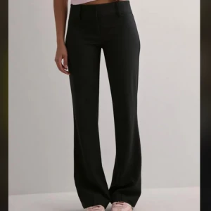 Svarta bootcut kostymbyxor från Nelly - Snygga svarta kostymbyxor från Nelly i storlek 34. Byxorna är bootcut och har låg midja. Materialet är mjukt och har en lätt stretch för skön passform. Perfekta för dig som gillar stilrena och trendiga byxor.