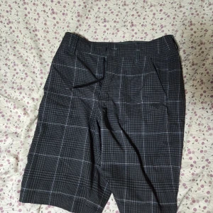 Svarta rutiga shorts Mossimo Supply - Snygga svarta shorts från Mossimo Supply Co med vitt rutmönster och snörning i midjan. Modellen är loose fit och har praktiska fickor fram. Perfekta för dig som gillar streetstyle och vill ha en chill look. Materialet känns lätt och bekvämt.