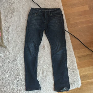 Mörkblå slim jeans Jack & Jones - Snygga mörkblå jeans från Jack & Jones med slim passform. Modellen heter Glenn och har klassisk femficksdesign, snygga slitningar och detaljerade sömmar. Perfekt för dig som gillar en slim och stilren look. Storlek 27:30