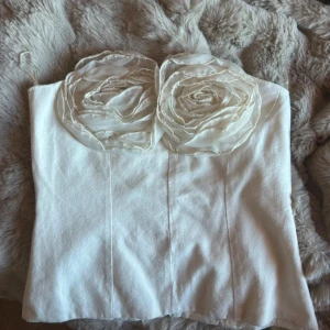 Vit tubtopp med rosdetaljer från Zara - Superfin vit tubtopp från Zara med två stora rosdetaljer framtill. Toppen är axelbandslös och har en stilren, croppad passform. Helt ny.