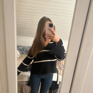 Svartvit randig stickad tröja - Säljer en svart stickad tröja med breda vita ränder. Tröjan har v-ringad hals, långa ärmar med ribbade muddar och en loose passform. Perfekt för dig som gillar chill och oversized stil. Materialet är mjukt och skönt stickat.