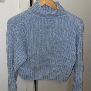 Ljusblå ribbad polotröja - Säljer en ljusblå ribbad polotröja med croppad passform och lång ärm. Tröjan har en hög krage och är stickad i mjukt material som känns skönt mot huden. Perfekt för dig som gillar chill och stilren vibe.