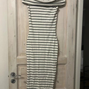 Randig offshoulder långklänning - Säljer en snygg långklänning med svartvita horisontella ränder och offshoulder-krage. Klänningen har en figurnära passform och är tillverkad i ett mjukt, ribbat material som ger en cool och modern look. Perfekt för dig som gillar stilrena och trendiga plagg.