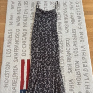 Leopardmönstrad långklänning från Gina Tricot  - Säljer en maxiklänning från Gina Tricot i leopardmönster med tunna axelband och snygg draperad halsringning. Klänningen har en loose passform och är tillverkad i mjuk polyester som känns skön mot huden. Perfekt för dig som vill sticka ut med ett djuriskt print.