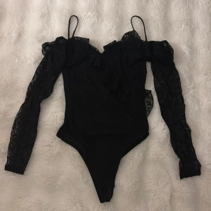 Svart spetsbody med volang från Topshop - Säljer en svart body från Topshop med långa spetsärmar och tunna axelband. Toppen har snygga volangdetaljer över axlarna och är offshoulder. Pris kan diskuteras