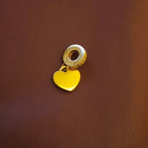 Pandora charm Guldigt hjärthänge till armband  - Snyggt hänge i guldton med hjärtformad berlock. Ringen har små gnistrande stenar runtom och hjärtat är slätt och blankt. Perfekt att sätta på ett armband eller halsband för en personlig touch.