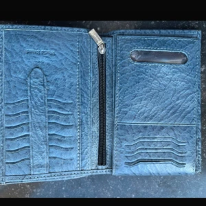 Blå läder plånbok från Maral - Snygg blå plånbok i läder från Maral med flera kortfack, fönster för ID och praktisk dragkedja för mynt. Plånboken har en cool textur och levereras i originalask. Perfekt för dig som vill ha ordning på kort och cash. Helt ny.
