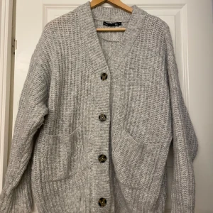 Grå stickad kofta med stora knappar - Mysig grå oversized stickad kofta med stora dekorativa knappar framtill och två rejäla fickor. Koftan har en loose passform och långa ärmar, passar även s och m