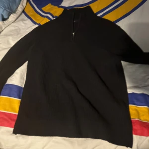 Svart stickad polotröja med half zip - Svart stickad polotröja med half zip i halsen. Tröjan har lång ärm och en ribbad struktur som ger en schysst look. Perfekt för dig som gillar stilrena och enkla plagg med lite edge. Passar dig som vill ha en varm och snygg tröja till kyliga dagar.