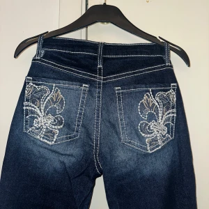 Mörkblå YMI jeans med broderade fickor - Snygga mörkblå jeans från YMI med kontrasterande vita sömmar och broderade detaljer på bakfickorna. Modellen har bootcut-ben och låg/mid midja, tillverkade i klassiskt jeansmaterial. De är tyvärr för korta för mig som är 170cm💕🎀🌸 Öppen för prisförslag!❤️
