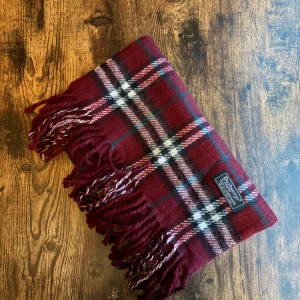 Burberry halsduk - Klassisk Burberrys-halsduk i 100% lammull, tillverkad i England. Mjukt och varmt material i ikoniskt rutmönster. Passar både dam och herr. I mycket bra skick små fläckar eller utan hål – perfekt för höst och vinter. 