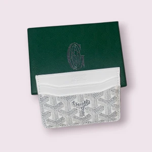 Vit plånbok med mönster  - Snygg och stilren vit plånbok  med ikoniskt mönster och logotyp framtill. Plånboken har flera fack för kort och är tillverkad i exklusivt skinn. Kommer i original grön ask med silverdetaljer. Perfekt för dig som gillar lyxiga accessoarer.