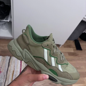 Adidas sneakers i olivgrönt och beige - Säljer ett par feta Adidas sneakers i olivgrönt och beige med vita ränder och gröna detaljer. Skorna har chunky sula, snörning och är gjorda i en mix av mocka och syntet. Perfekta för dig som vill sticka ut med en unik färgkombo och skön streetstil.