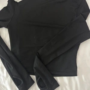 Svart långärmad tröja med tumhål - Svart långärmad tröja med tumhål i ärmsluten. Tröjan croppad och går ungefär till magen, alltså täcker inte hela magen. 