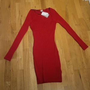 Röd ribbad klänning från H&M - Röd, tight ribbstickad klänning från H&M med lång ärm och assymetrisk halsringning. Klänningen är kort och har en figurnära passform som framhäver siluetten. Perfekt för dig som gillar en enkel men snygg look.