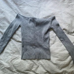 Grå offshoulder långärmad topp - Säljer en stilren grå offshoulder topp med lång ärm. Toppen har en tight passform och är perfekt för dig som gillar minimalistisk stil. Materialet är mjukt och stretchigt, vilket gör den skön att bära. Enkel att matcha med både jeans och kjol. Köpt secondhand 🩵