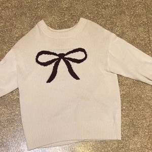 Beige stickad tröja med rosett från Ginatricot - Supersöt beige stickad tröja från Gina Tricot i storlek 158/164. Tröjan har ett stort mörkbrunt rosettmotiv framtill och ribbade muddar vid hals, ärmslut och nederkant. Kom gärna med prisförslag! Nypris: ca 250 kr