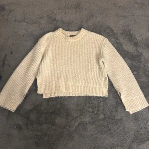 Beige croppad stickad tröja Gina Tricot - Säljer en beige croppad stickad tröja från Gina Tricot. Tröjan har grov ribbstickning, rund hals och långa ärmar med breda muddar. Perfekt för dig som gillar en chill och trendig look med lite kortare passform.